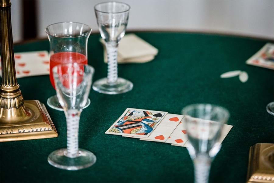 A table surface with playing cards, stemmed drinking glasses and the gold base of a lamp