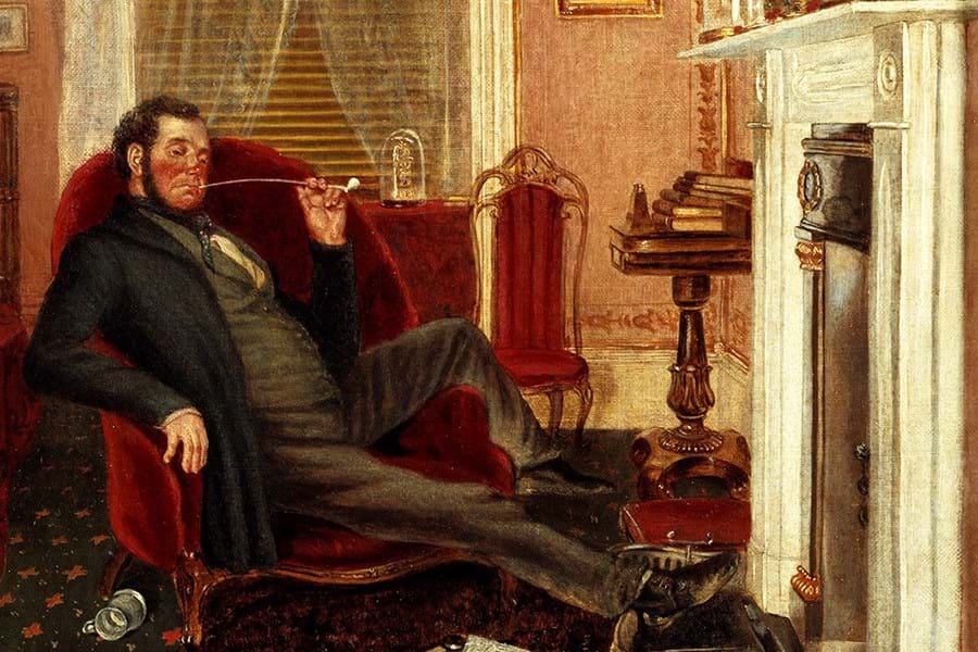A person sat on a red armchair, smoking a pipe with feet by the fire