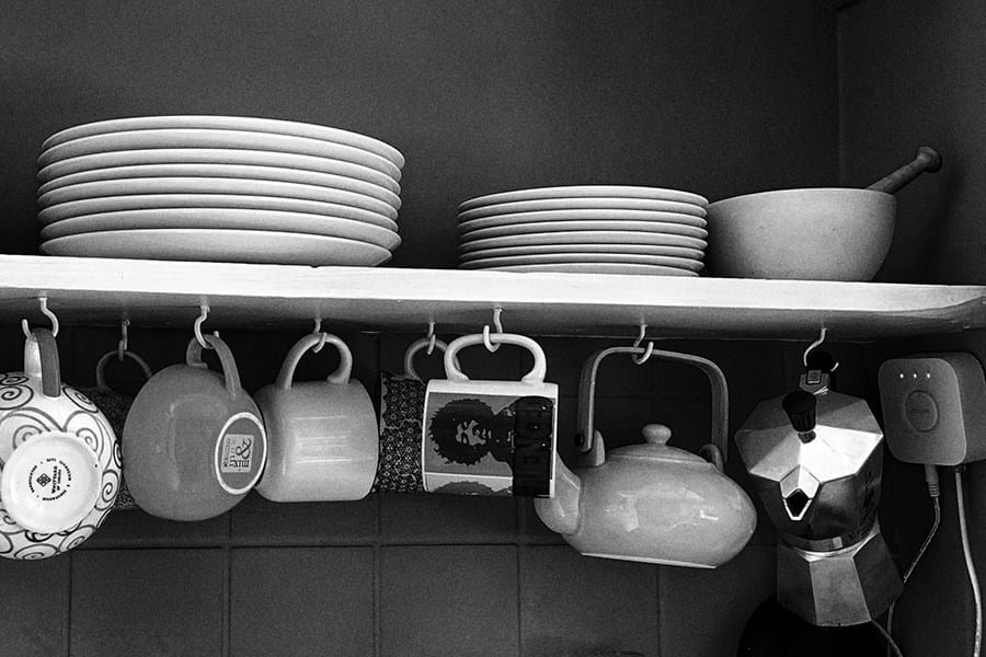 Plates piled on a shelf with mugs hanging underneath