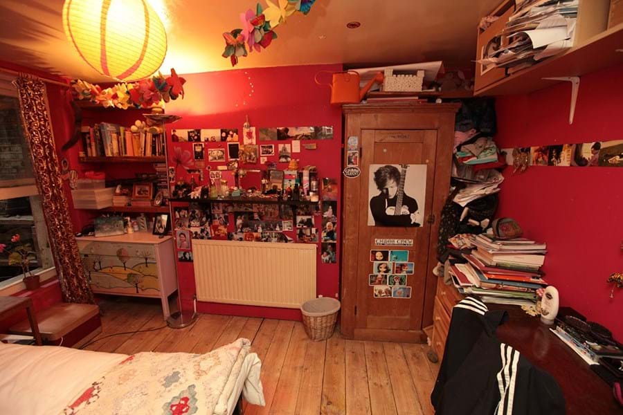 Colour photograph of a bedroom with red walls and posters and photos on the wall