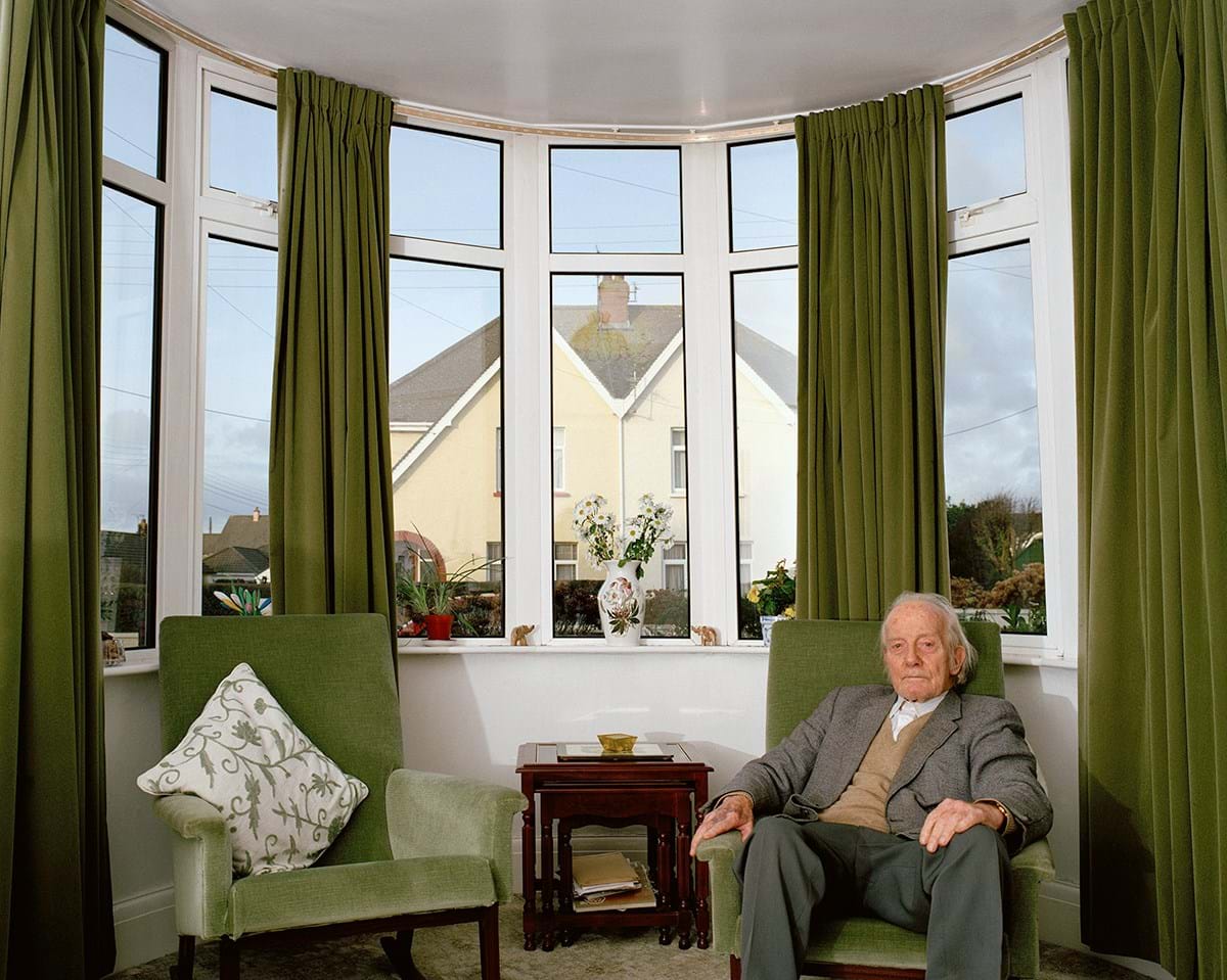 A person sitting on a green sofa in front of windows with green curtains 