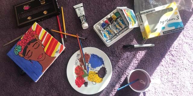 Various paints and paintbrushes next to a small canvas