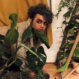 Person crouching on the floor surrounded by plants