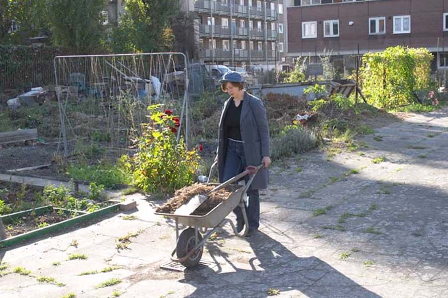 Kate Poland pushing a wheelbarrow along a path in an allotment