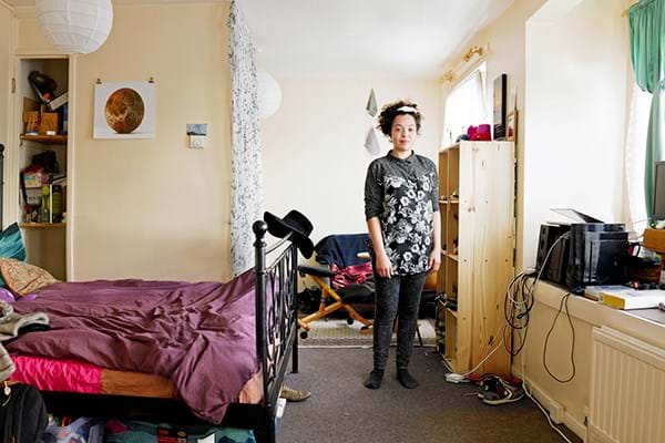 A person standing in a bedroom between a bed and a shelving unit