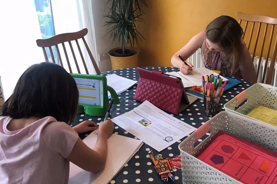 Two children sat at table doing school work 