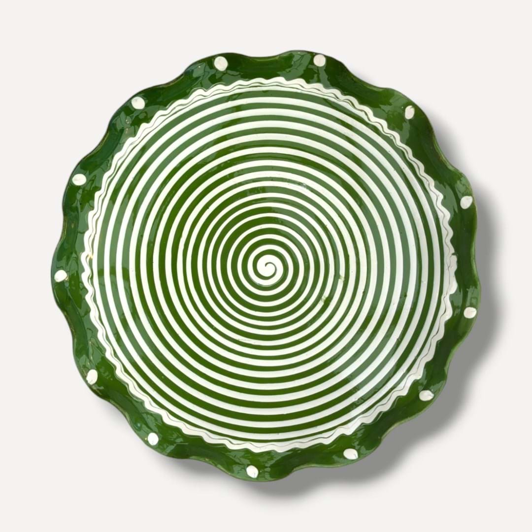 A handmade ceramic plate with a rippled edge, decorated with green paint in a spiral pattern
