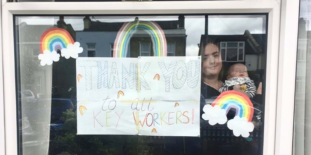 A person holding a baby behind a window with posters of rainbows in front 