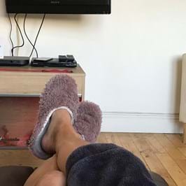 The photographer's legs, resting on a low table, wearing fluffy slippers, in front of a television