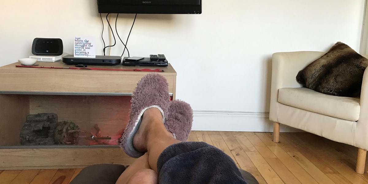 The photographer's legs, resting on a low table, wearing fluffy slippers, in front of a television