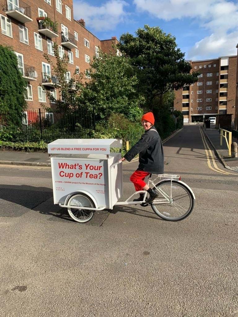A person riding a bike cart displaying the words 'What's your cup of tea?' 