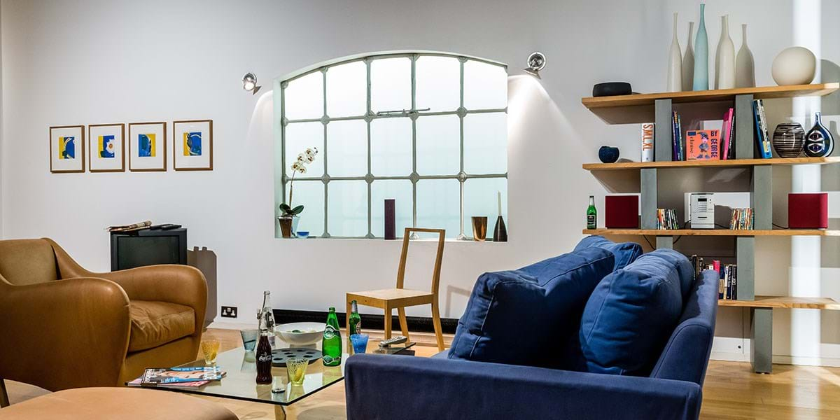 Room with wooden floor, blue sofa and mustard coloured armchair and glass coffee table