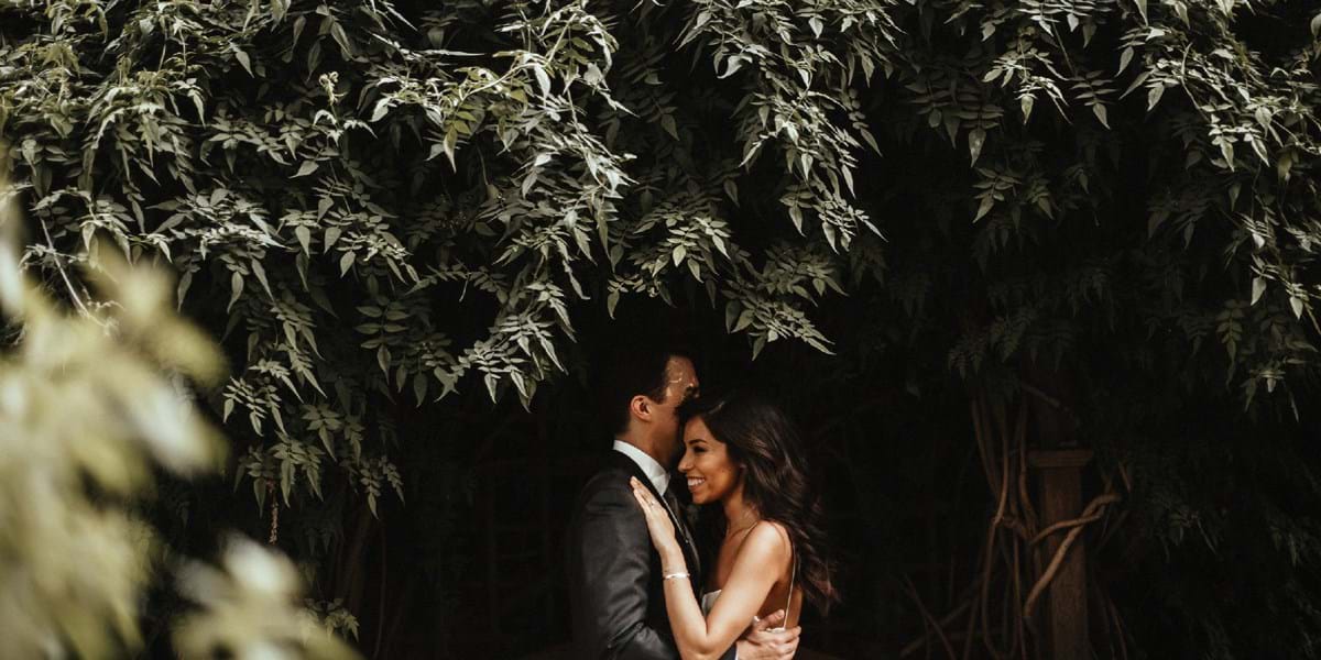 Two people embracing in front of a hedge