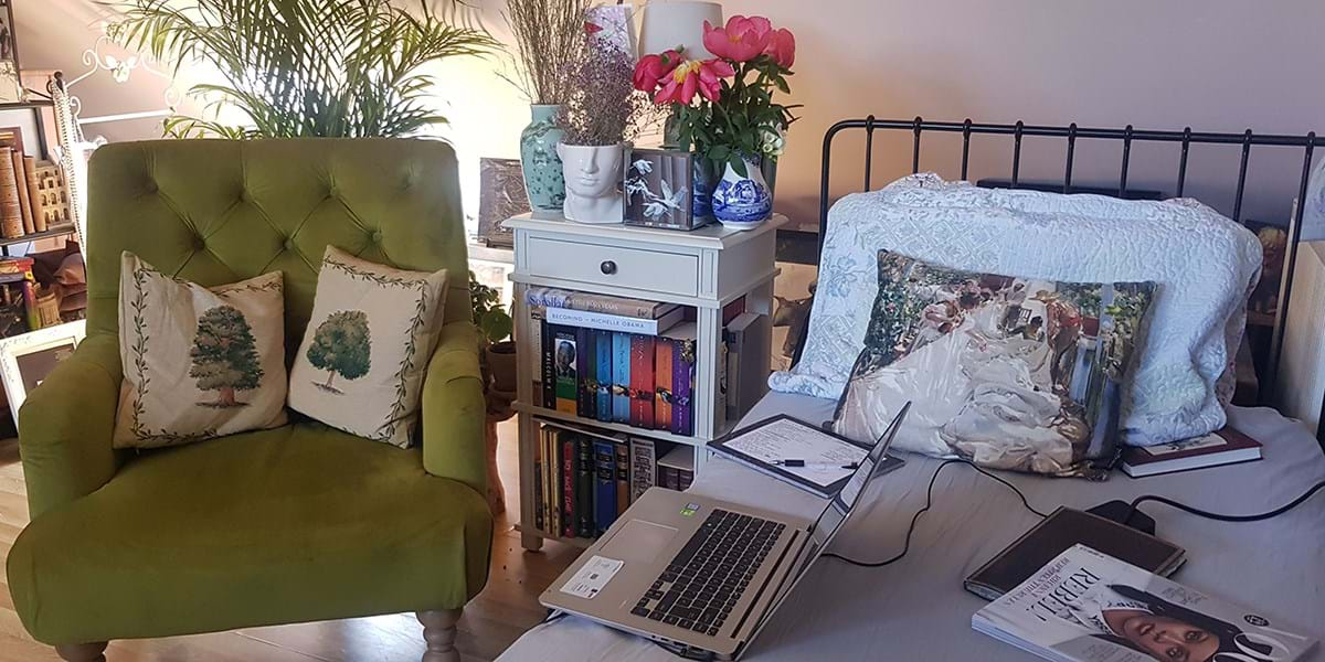 A green armchair with two cushions next to a bed with an open laptop on it