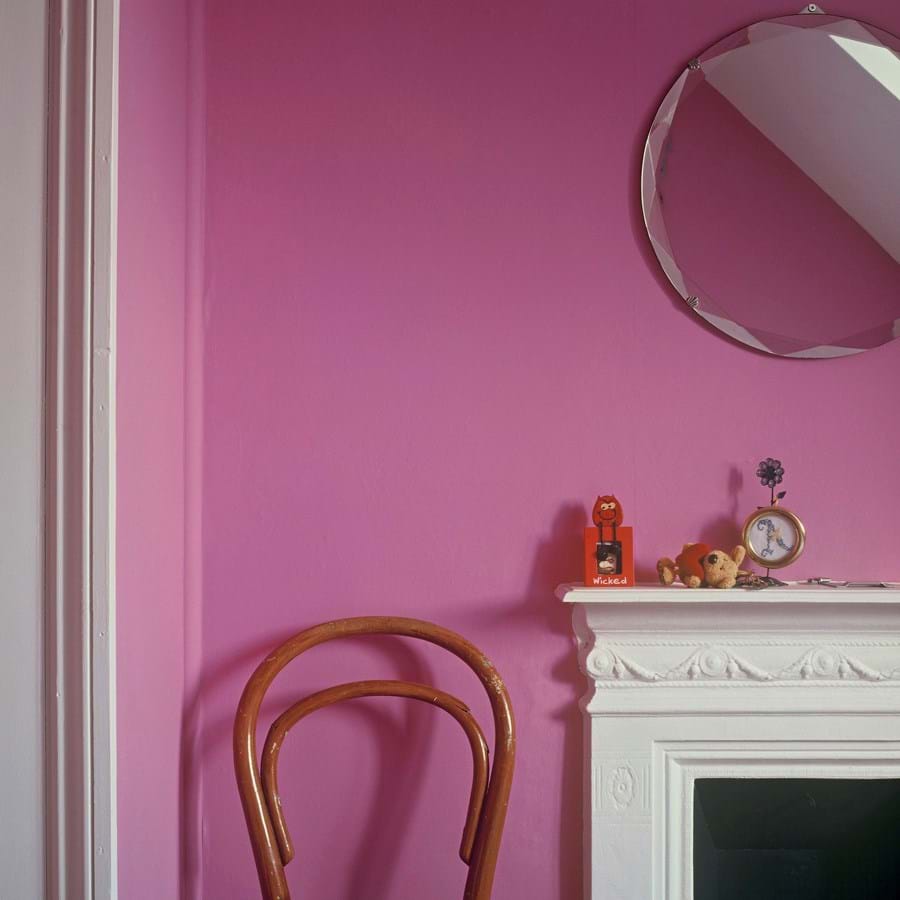 Circular mirror over a white mantelpiece against a dark pink wall