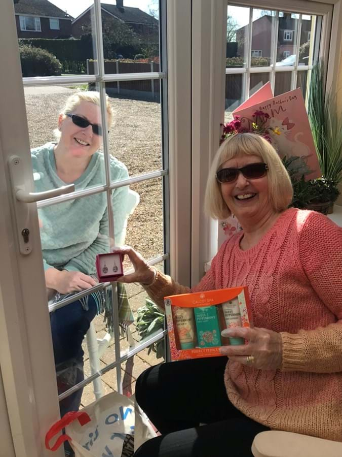 Two people sat on either side of a closed glass door, one is holding gifts 