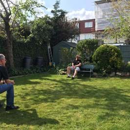 Four people socially distancing in a garden, two on stools, one on a bench and one standing