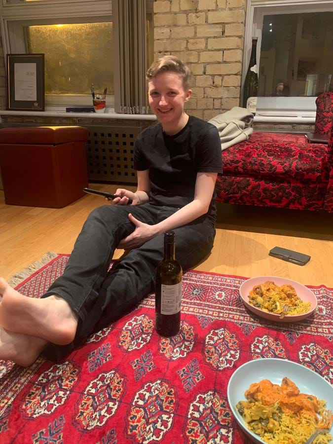 Person sitting on a red rug next to a plate of food and a bottle of wine