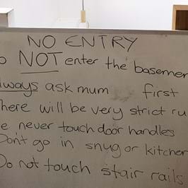 A white board that reads 'No Entry: do not enter the basement. Always ask mum first. There will be very strict rules: i.e. never touch door handles. Don't go in snug or kitchenette. Do not touch stair rails.'