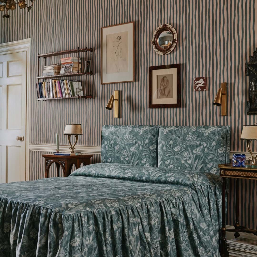 A bedroom decorated with wall paper, bronze light features and blue floral bedding