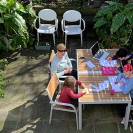 A group of adults and children sat round in a table in a garden