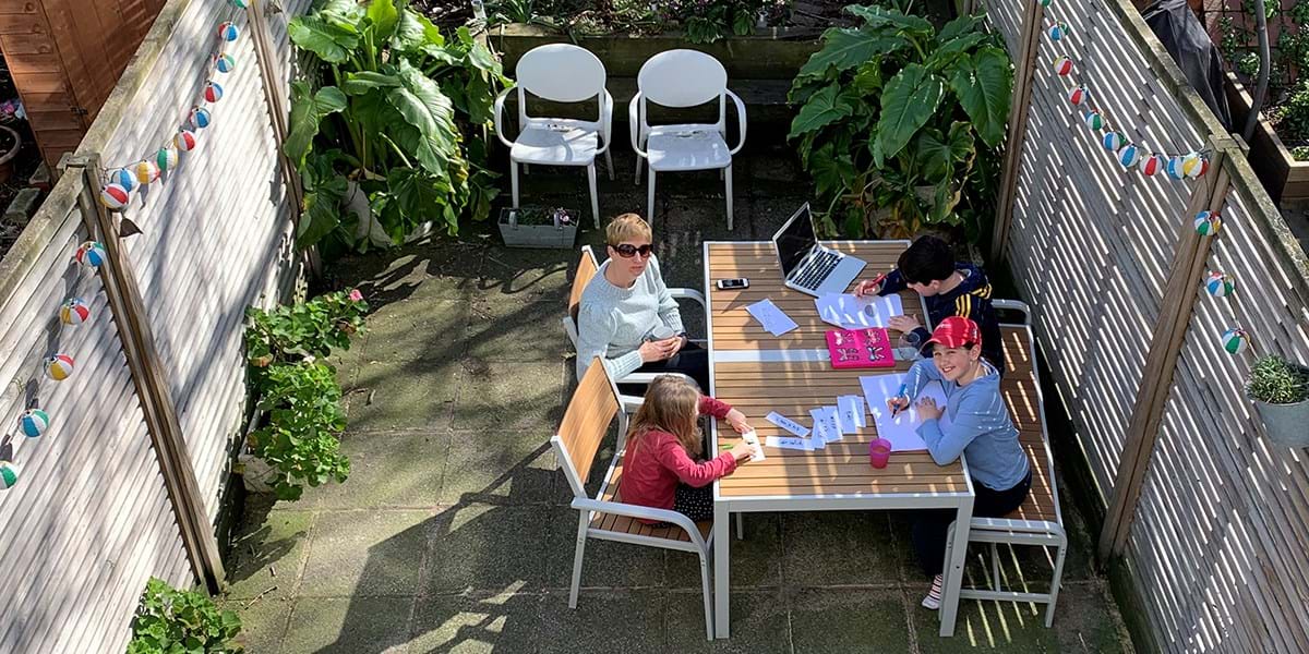 A group of adults and children sat round in a table in a garden