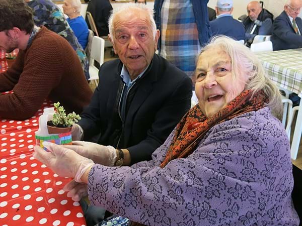 Two older people sat at a table holding up small plants