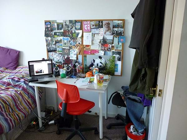 A bedroom with a desk and a noticeboard 