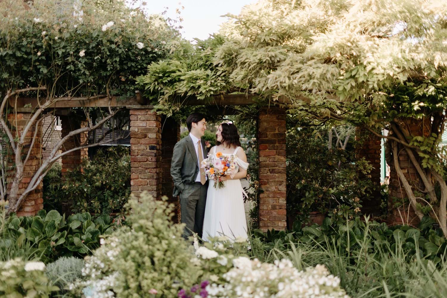 A couple getting married under an arch made of bricks and plants