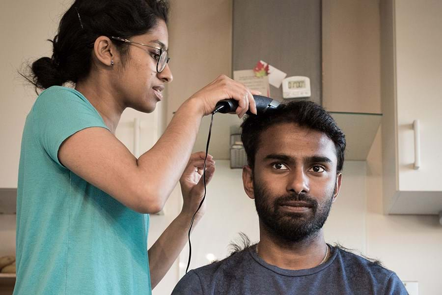 A person standing giving a seated person a haircut