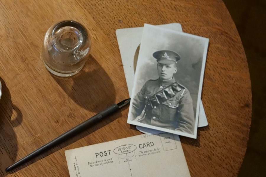 A wooden table set with a glass, a postcard and a black and white photo of a person in military dress