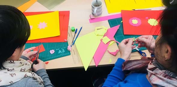 People cutting out shapes from coloured paper at a desk