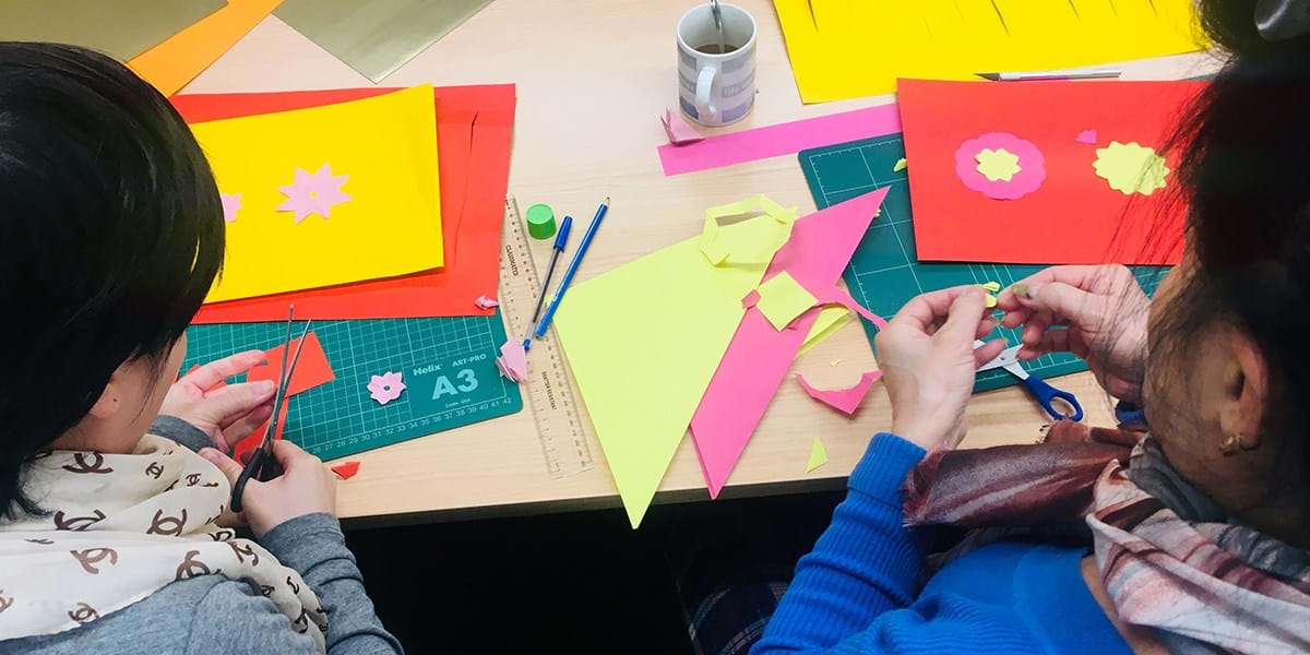 People cutting out shapes from coloured paper at a desk