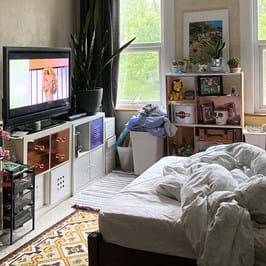 An unmade bed facing a tv, on top of shelves of books 