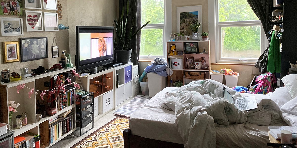 An unmade bed facing a tv, on top of shelves of books 