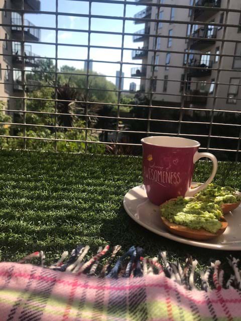 Slices of toast with avocado on a plate, next to a red mug