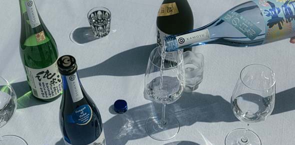 Bottles of sake being poured into crisp wine glasses, set on a white tablecloth