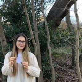 A person holding a piece of paper standing in front of a tree