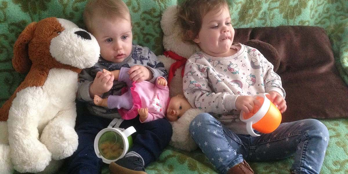 Two children sat together surrounded by soft toys