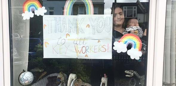 Person holding a baby behind a window decorated with posters of rainbows