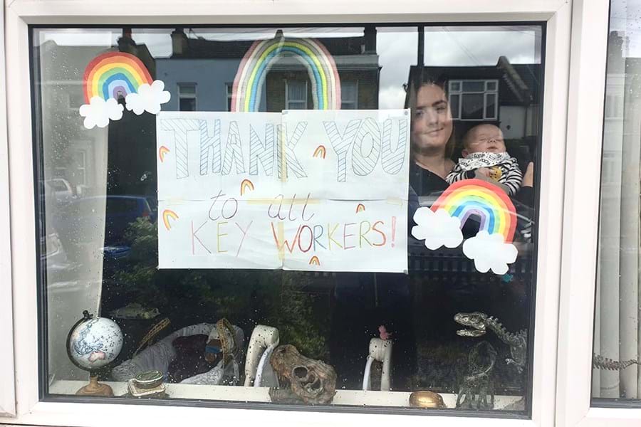 Person holding a baby behind a window decorated with posters of rainbows