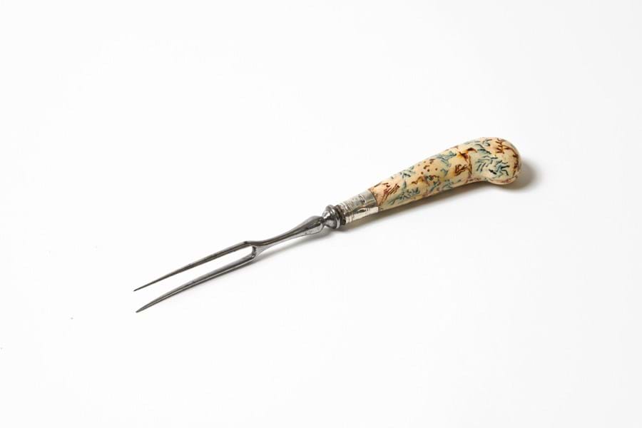 A metal two-pronged fork with a cream handle, decorated with colourful patterns