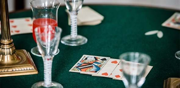 A table surface with playing cards, stemmed drinking glasses and the gold base of a lamp