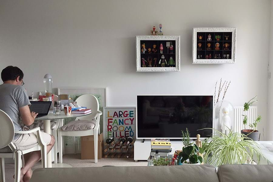 Person sat at a table next to a large television set and plants