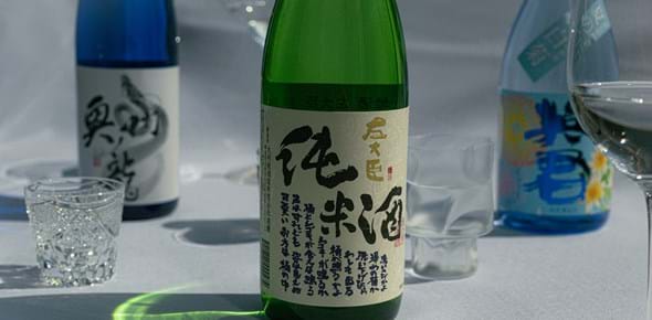 Bottles of sake and clear wine glasses, set on a white tablecloth