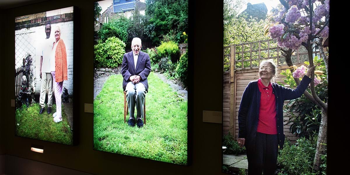 Three images of people standing in their gardens, display on lightboxes