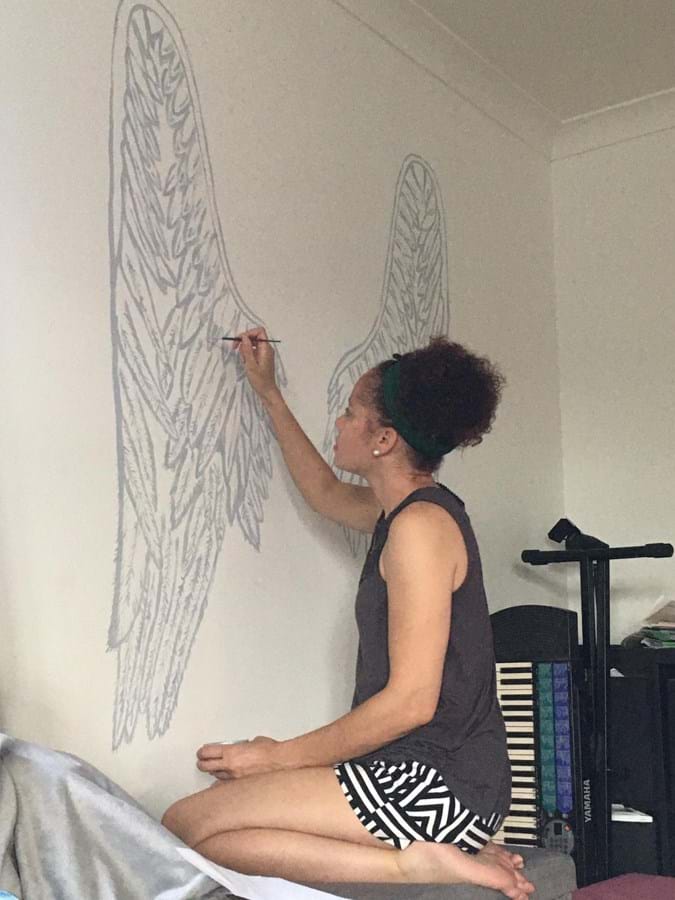 Person sat in kneeling position painting a large pair of wings onto a wall