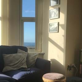 A view of the sea out of the window with a sofa and shelving unit in the foreground