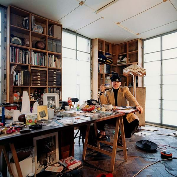 A person sat at a long desk covered in books and objects 