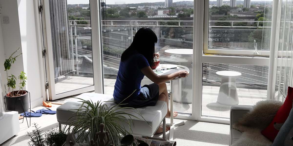 Person sitting while eating and reading in front of a window with view of train tracks